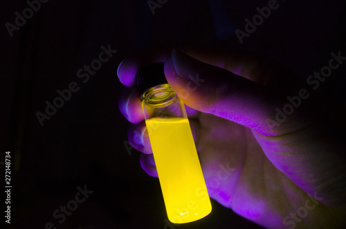 Woman researcher holding yellow photochemical reaction in glass vial under UV light in a dark chemistry laboratory photo