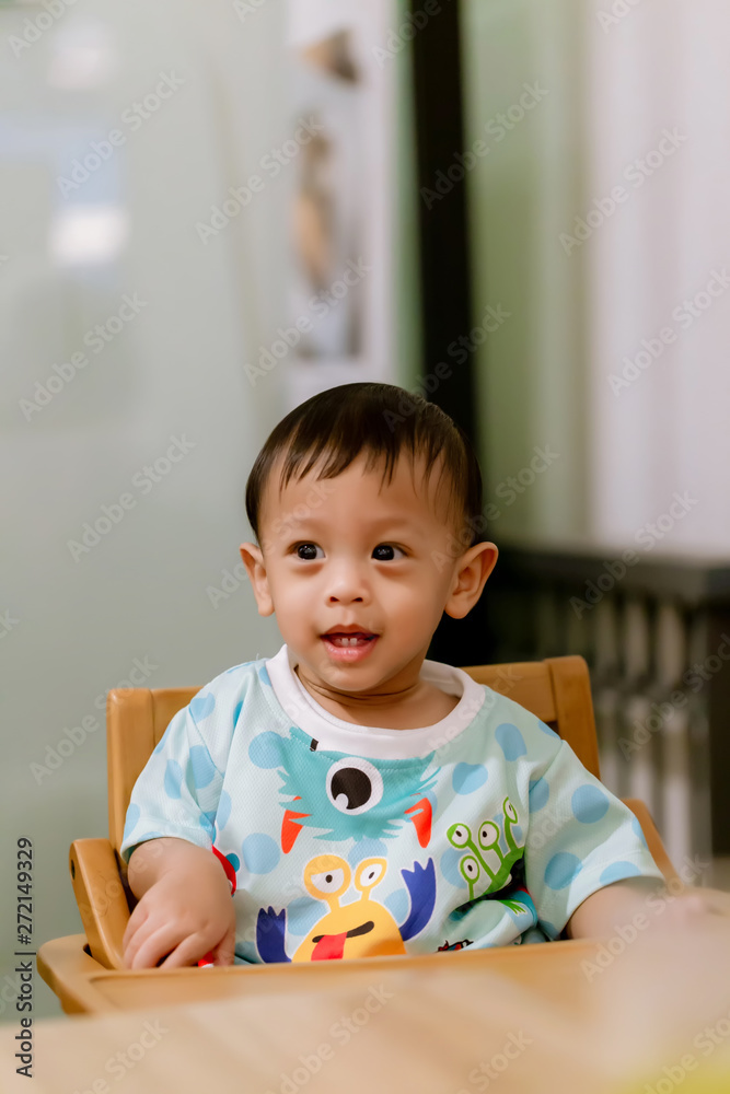 Portrait Of Happy Young Baby Boy In High Chair. Child sitting at empty table.Baby nutrition concept.Food advertisement design. smiling baby sitting on baby Chair. Portrait Of Happy Young Baby Boy In High Chair. Child sitting at empty table.Baby nutrition concept.Food advertisement design. smiling baby sitting on baby Chair.