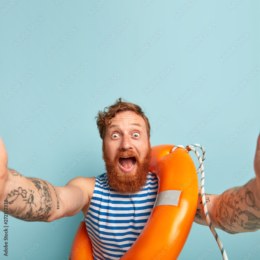 Impressed happy surprised male swimmer shouts at camera, stares with bugged eyes, makes selfie, learns lifesaving skills and how to overcome potential hazards, poses with lifebuoy, stands indoor - obrazy, fototapety, plakaty 