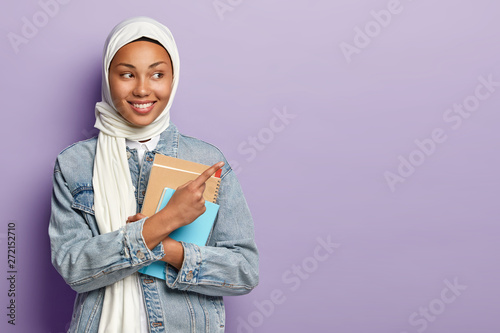 Canvas Print Isolated shot of satisfied Muslim student shows awesome advert, points at upper