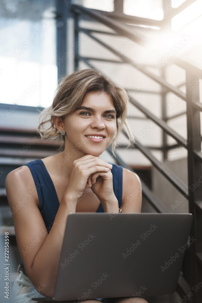 Fototapeta premium Vertical close-up shot attractive happy smiling blond european young woman sit stairs outdoor hold laptop knees working freelance, studying, gather information before classes research via internet