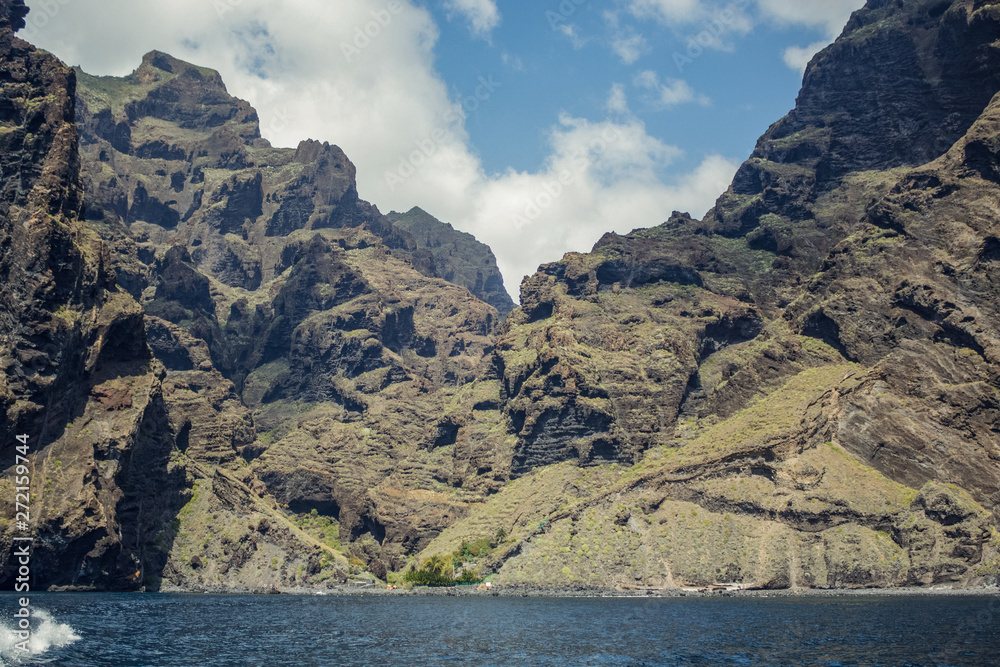 Steep high lava rock cliffs. Blue sea horizon, natural sky background.