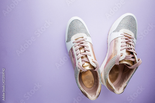 Fashion blog look. White women's sneakers with pink and gold color on purple background. Flat lay, top view beauty female background.