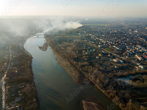 Aerial top view of river flowing through town. Rural landscape of residential house roofs, roads and tree tops on spring or autumn day. Drone photography. © bilanol