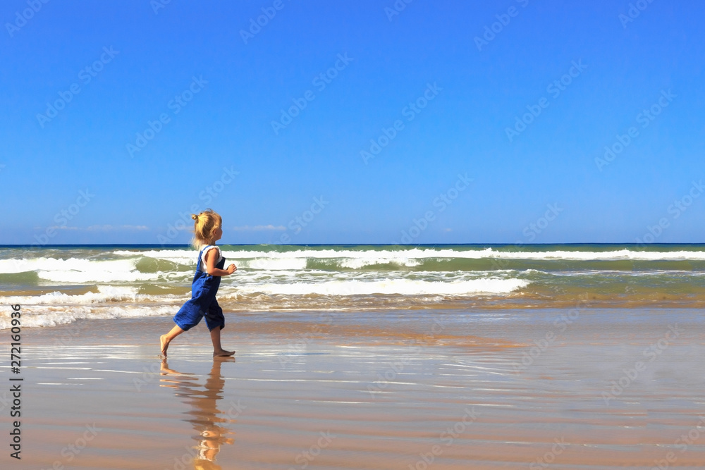 The girl is walking along the beach on a sunny day.