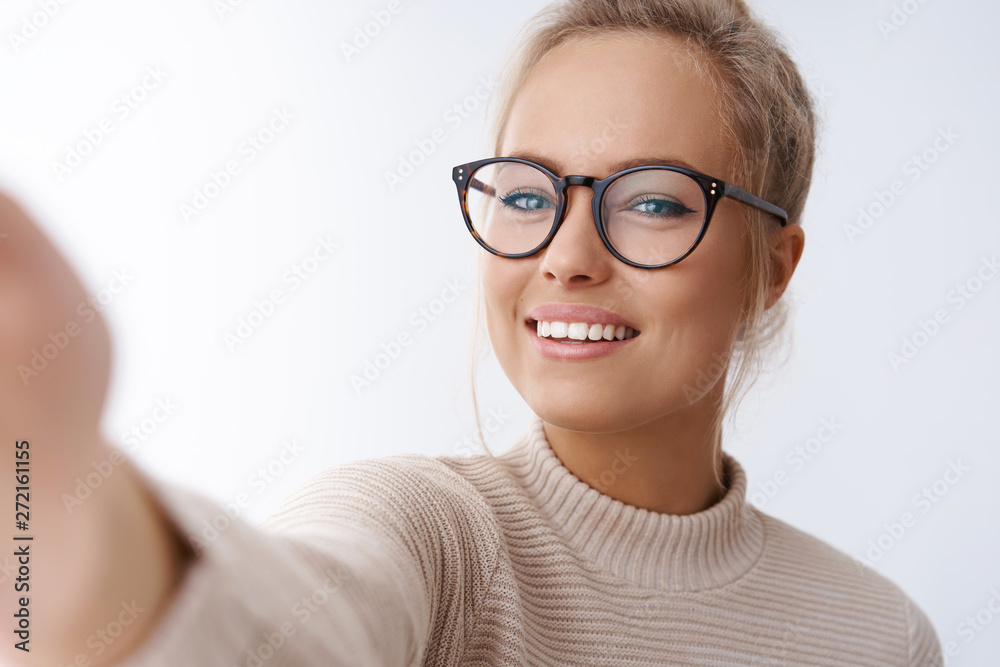 Close-up shot of charming female lifestyle blogger holding camera extend hand taking selfie making video call smiling broadly with happy and joyful attitude having fun against white background