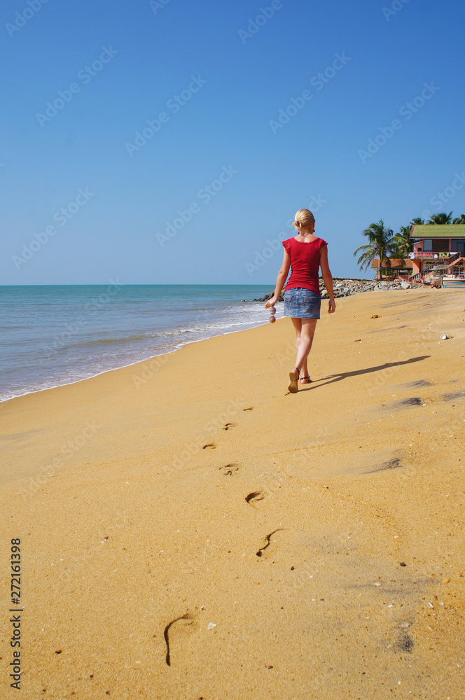 A girl walks along a sandy sunny beach in Sri Lanka. A girl walks along a sandy sunny beach in Sri Lanka.