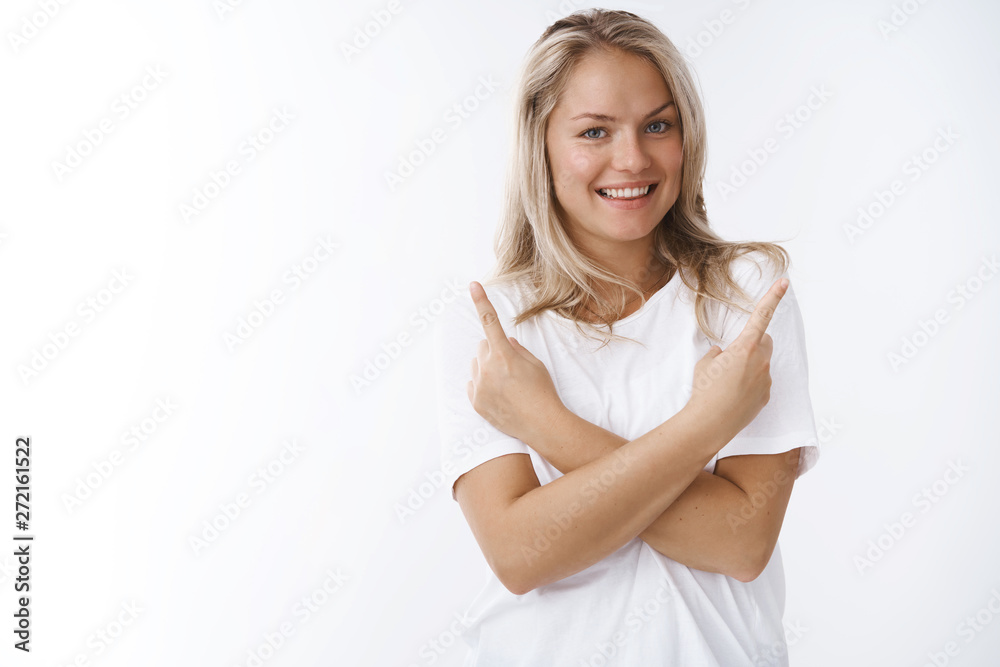 Which one. Studio shot of beautiful tender and feminine blond adult woman in white t-shirt cross arms pointing sideways at upper corners smiling positive suggesting variants choose, making decision Which one. Studio shot of beautiful tender and feminine blond adult woman in white t-shirt cross arms pointing sideways at upper corners smiling positive suggesting variants choose, making decision