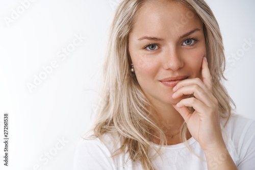Headshot of tender and sensual attractive european blonde in white t-shirt seducting touching lip flirty and smiling cheeky at camera posing feminine against white background