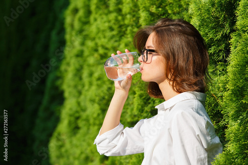 Young woman drinks water in garden