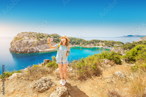 Asian Girl in a hat takes a selfie on the background of stunning views of the azure Bay in the Mediterranean sea. Travel, vacation and mobile connection concept