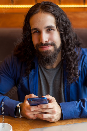 Wallpaper Mural Close up portrait of cheerful handsome intelligence young adult man freelancer in casual style sitting in cafe, holding phone and looking at camera, bussinessman in office. Indoor, lifestyle concept Torontodigital.ca