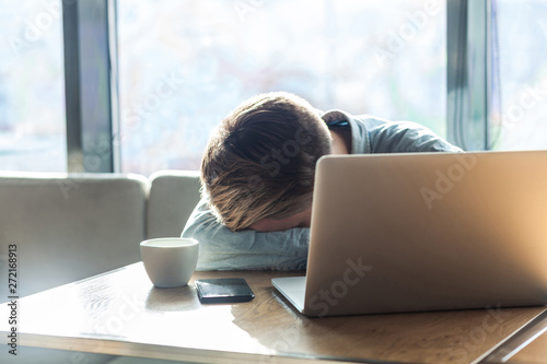 Obraz na plátně Portrait of sadness depressed tired young freelancer man in blue shirt are sitting alone in cafe and sleeping on the table after hard work, overtime work