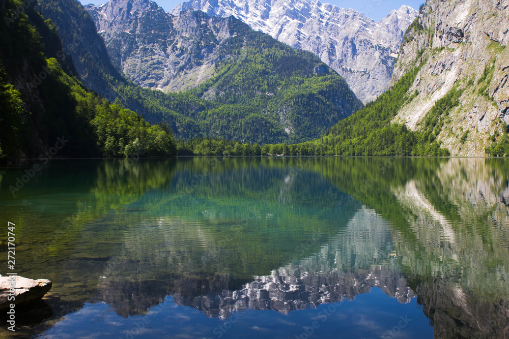 lake with crystal clear water in the spring mountains. A small lake in the Alps view from one shore. Reflection of mountains in the water of alpine lake