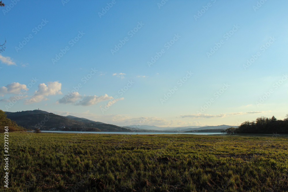 field and lake with beautiful blue sky and mountains