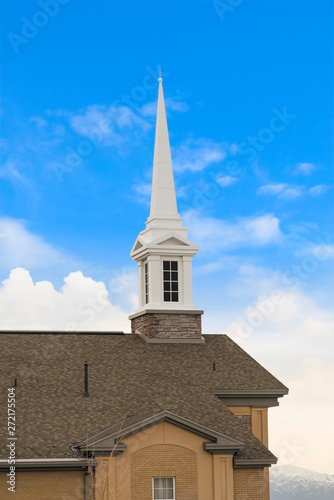 White steeple on top of the pitched roof of a church with brick exterior wall
