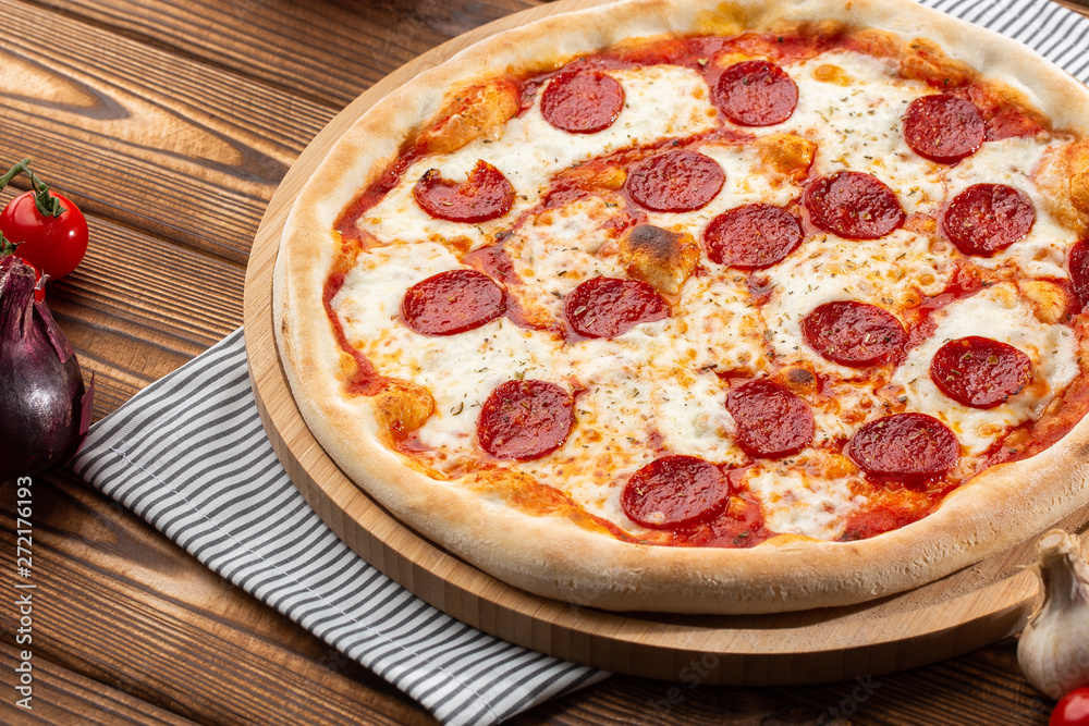 Delicious hot homemade Pepperoni pizza on the wooden table. Pepperoni Pizza - Fresh homemade pizza with pepperoni, cheese and tomato sauce on rustic black stone background wirh copy space.