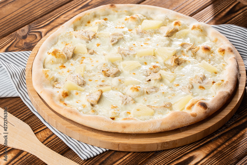 Pizza topped with sauce, chicken, cheese and pineapple serve on wooden plate on wooden table. Photo of Hawaiian pizza. Pizza topped with sauce, chicken, cheese and pineapple serve on wooden plate on wooden table. Photo of Hawaiian pizza.