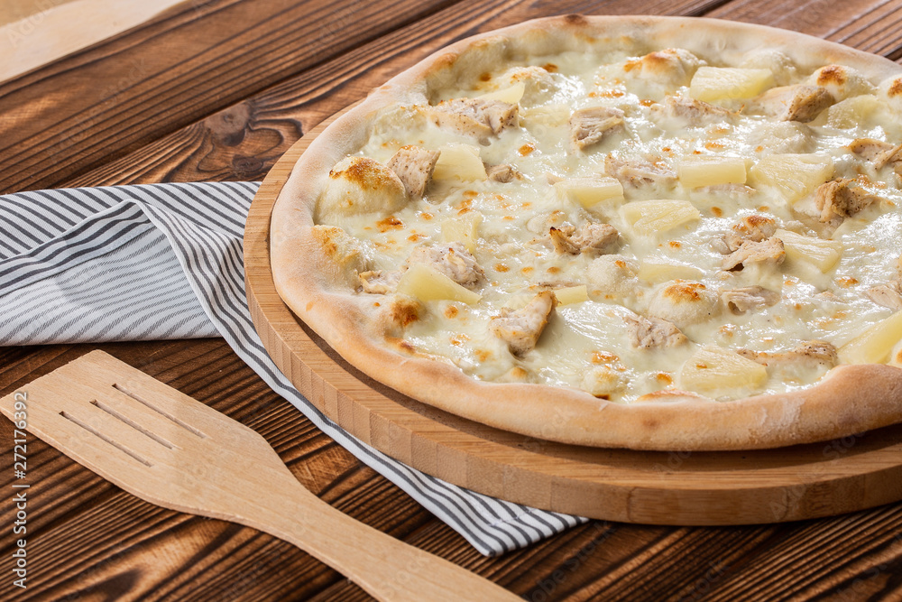 Pizza topped with sauce, chicken, cheese and pineapple serve on wooden plate on wooden table. Photo of Hawaiian pizza. Pizza topped with sauce, chicken, cheese and pineapple serve on wooden plate on wooden table. Photo of Hawaiian pizza.