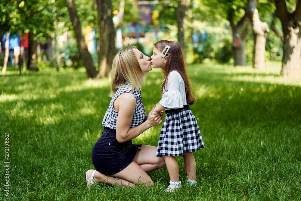 Happy mother and daughter kiss each other in the park.