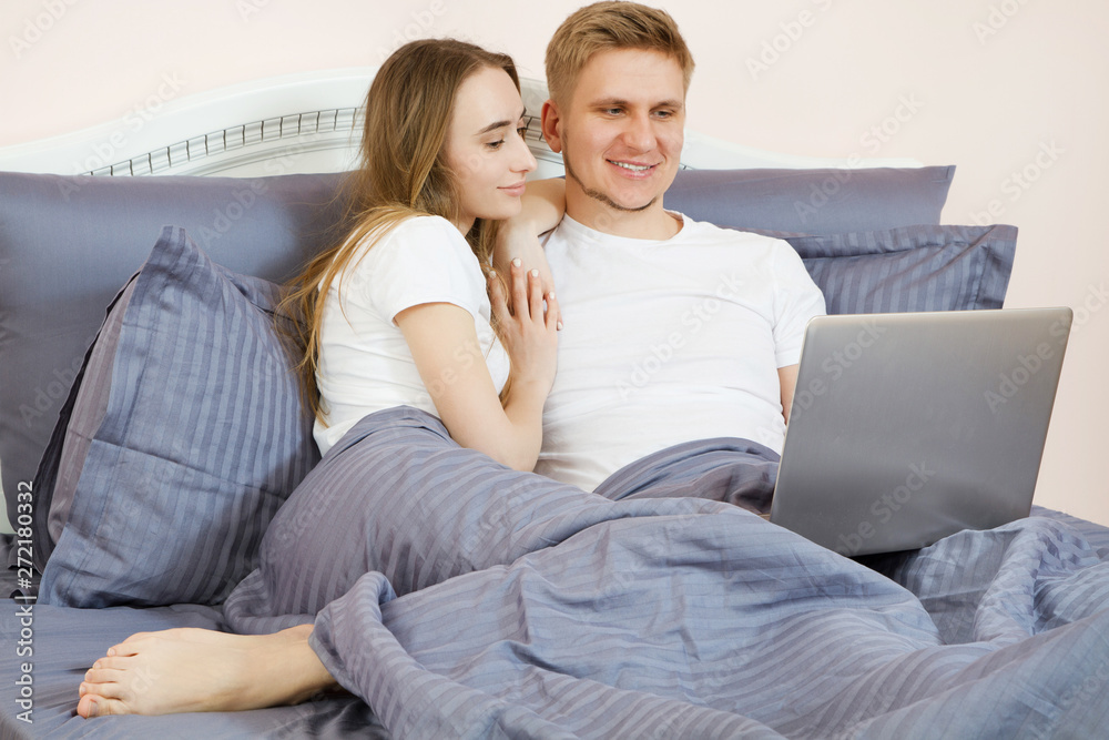 Young beautiful couple lying on bed in bedroom and using laptop Young beautiful couple lying on bed in bedroom and using laptop
