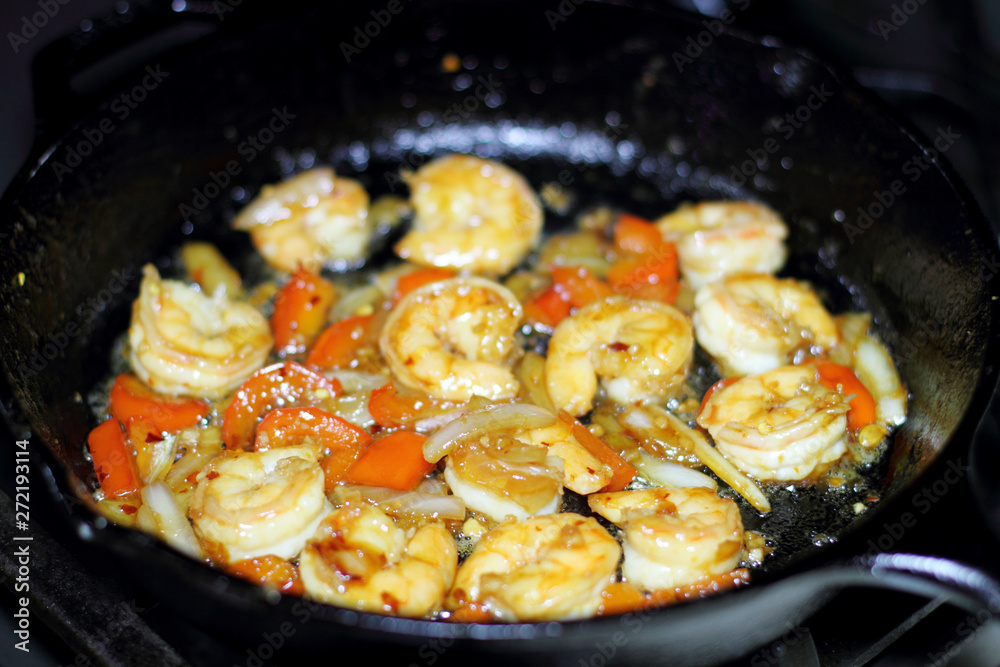Shrimp cooking with red bell peppers and onion in a cast iron skillet on the stove. Shrimp cooking with red bell peppers and onion in a cast iron skillet on the stove.