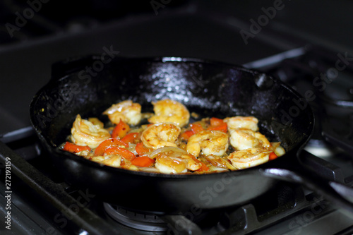 Shrimp cooking with red bell peppers and onion in a cast iron skillet on the stove.