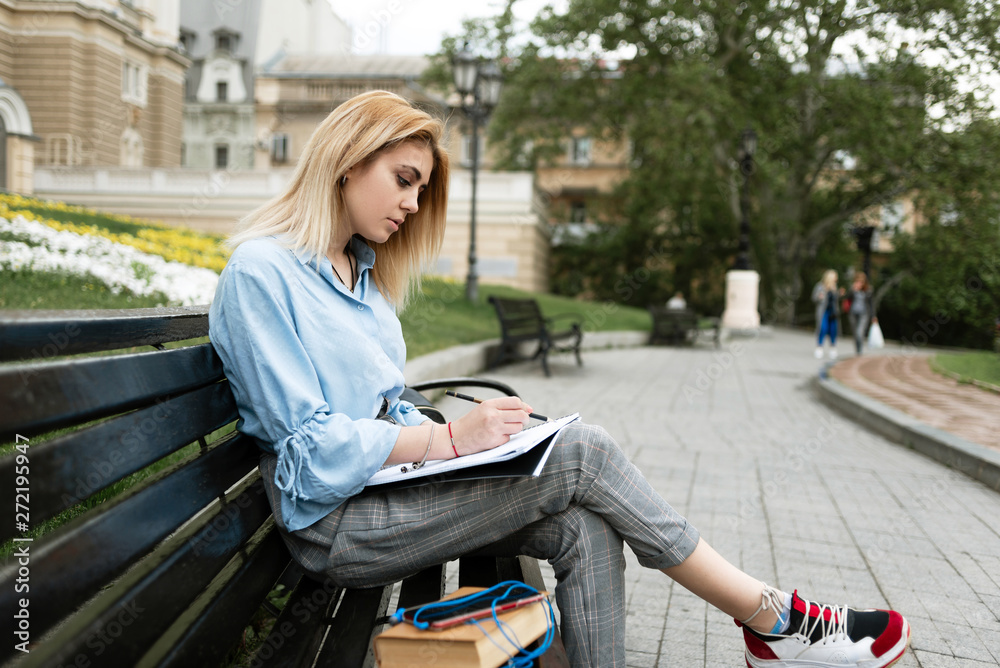 Fototapeta premium a creative girl sits on a bench and draws drawings in her sketchbook.