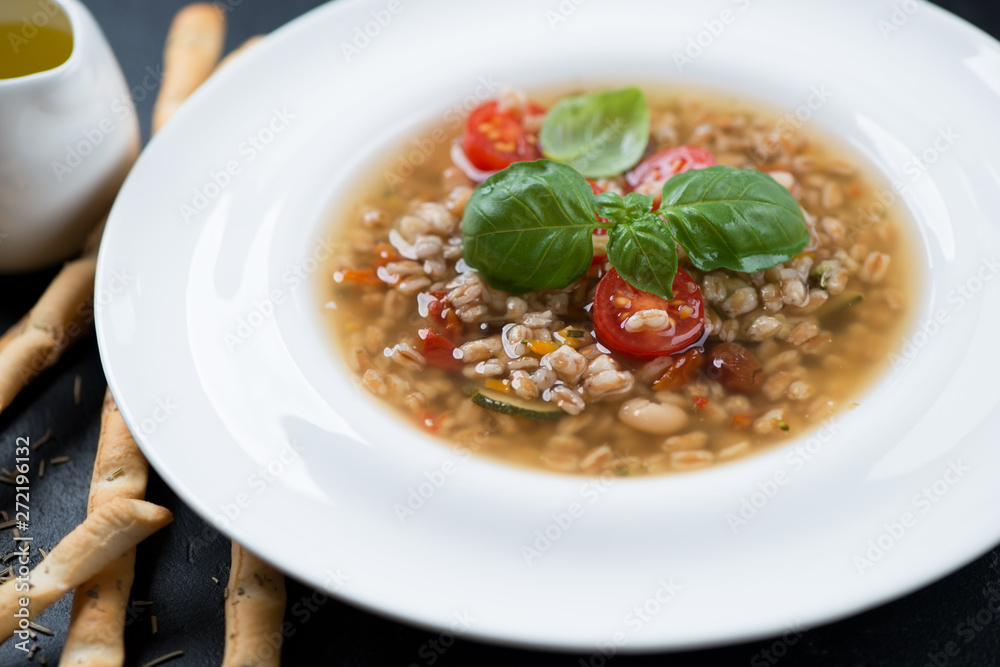 Close-up of italian spelt and vegetable soup served in a white plate, selective focus