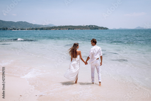 embracing romantic couplein white clothes looking on the sea on the Beautiful tropical beach vacation. Sea landscape with thai boat. Phuket. Thailand. Back view.