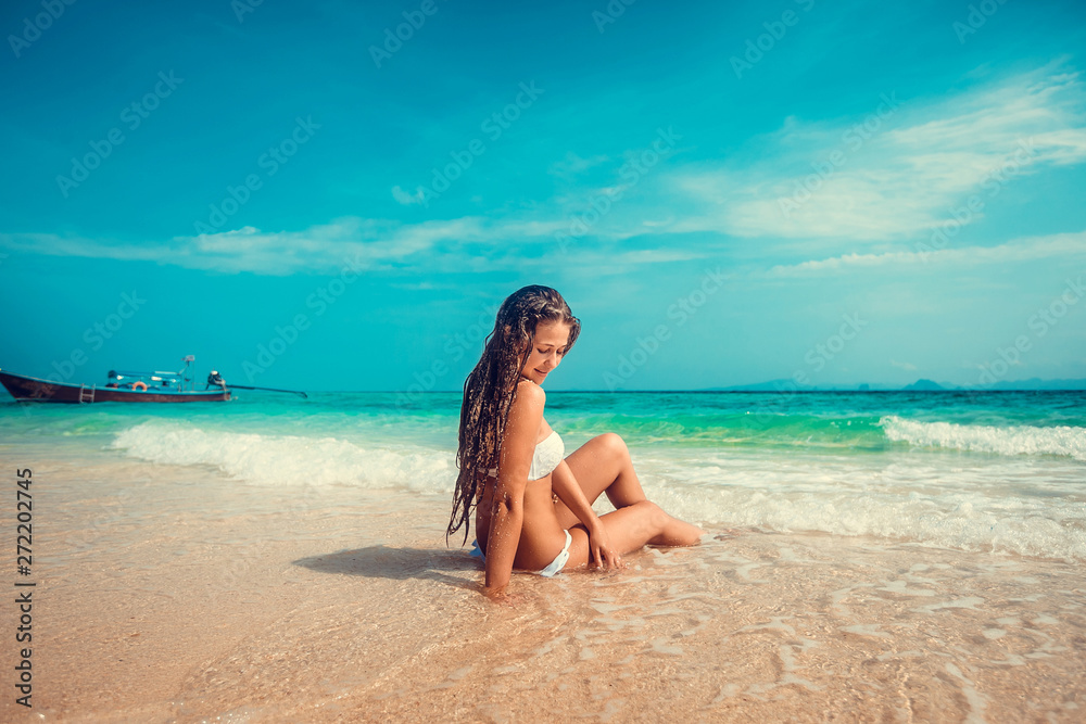 Young and pretty girl model in a bikini sunbathing on the beach resort of the Andaman sea. Boat and blue sea background