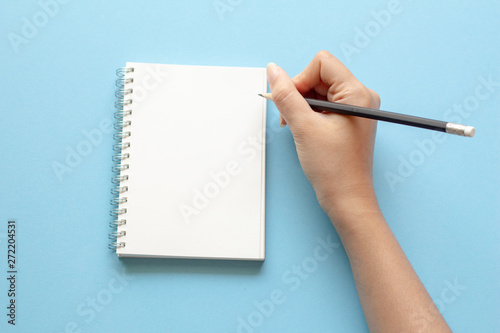 woman hands writing in empty notebook at the blue desk. Flat lay top view. 
