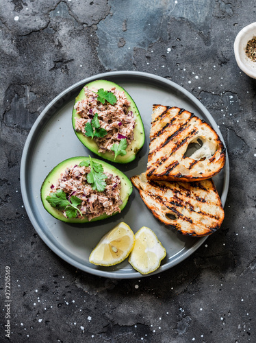 Tuna stuffed avocado - delicious healthy food on a dark background, top view