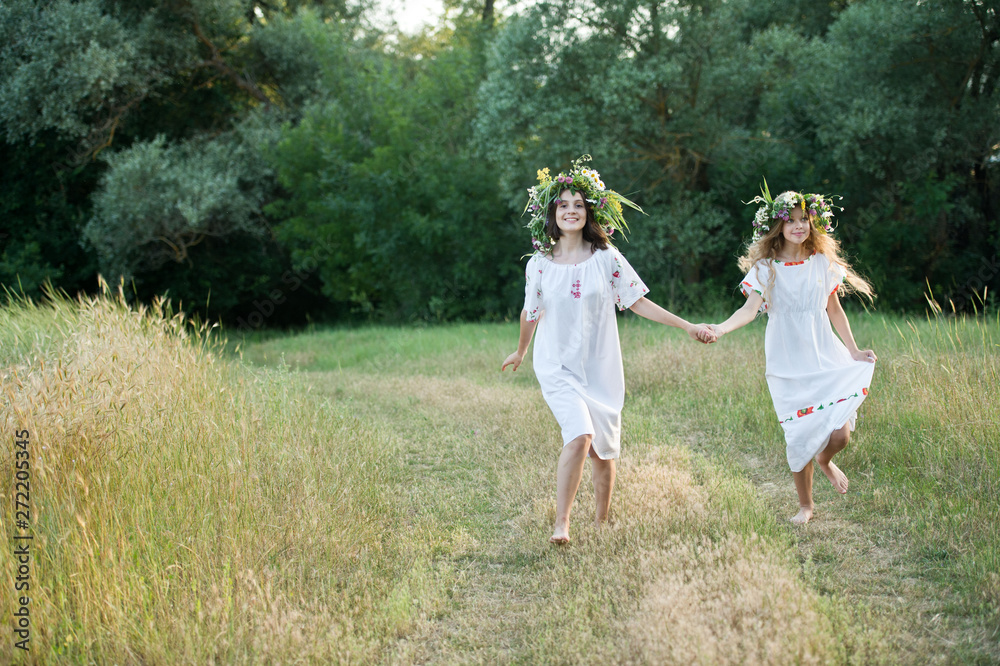 Two girls in wreaths from the field celebrate Ivan Kupala in the forest near the lake. The summer solstice Two girls in wreaths from the field celebrate Ivan Kupala in the forest near the lake. The summer solstice