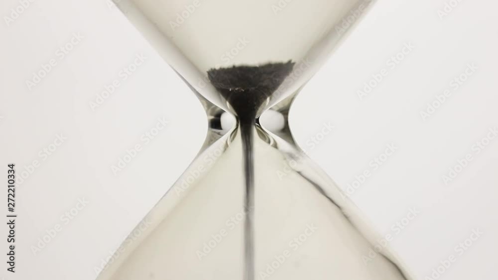Close-up of black magnetic powder flowing through a hourglass on white background