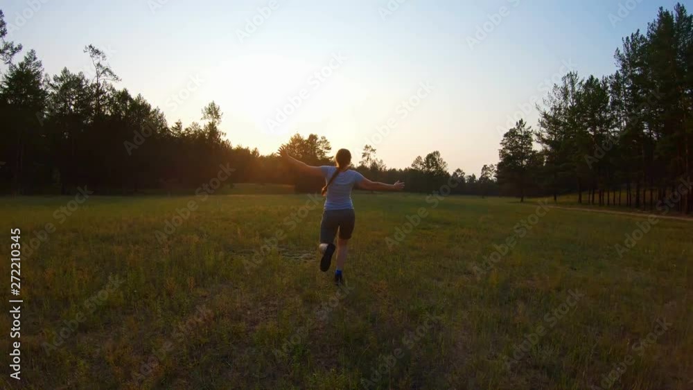 Cheerful girl, arms outstretched running across the field at sunset. Funny video, back view Cheerful girl, arms outstretched running across the field at sunset. Funny video, back view