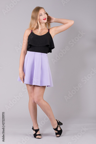 A young woman in summer clothes coquettishly posing on a light gray background.