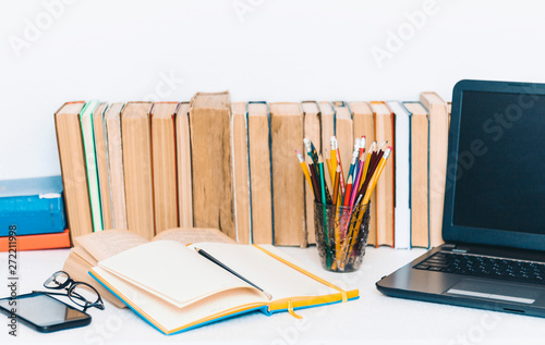 Open textbook, notebook, smartphone, laptop computer, stack of books education back to school background, glasses and pencils in plastic holder with copy space for text.