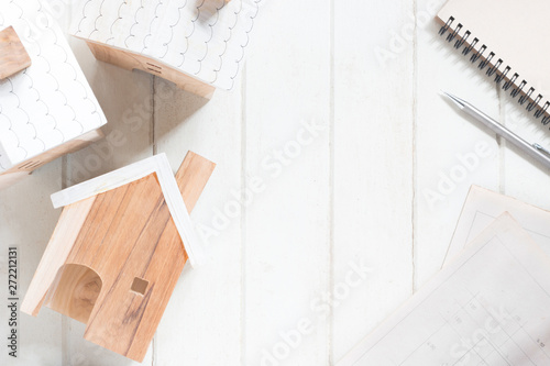 Miniature house model with house plan, pencil and notebook on white wood background, copy space