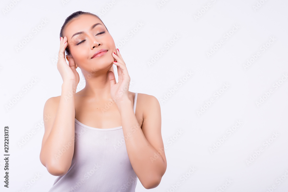Asian girl with healthy skin wearing a white singlet standing isolated over white wall background. With a smile Her eyes closed and hands touching the face expression of beautiful skin with copy space Asian girl with healthy skin wearing a white singlet standing isolated over white wall background. With a smile Her eyes closed and hands touching the face expression of beautiful skin with copy space