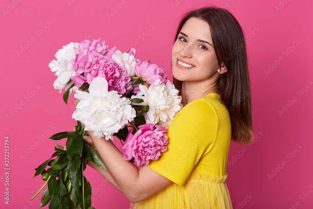 Close up profile portrait of attractive stylish woman in yellow casual t shirt isolated over oink studio background, holding peony flower bouquet, female with happy facial expression. Love concept. Close up profile portrait of attractive stylish woman in yellow casual t shirt isolated over oink studio background, holding peony flower bouquet, female with happy facial expression. Love concept.