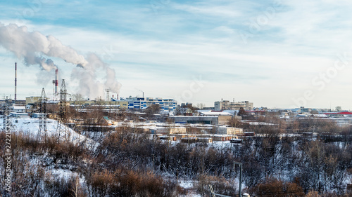 Outskirts Of Perm. In the foreground bushes and trees. In the depth of the picture we see the buildings of factories, Smoking pipes. On the right we see the support of high-voltage power lines.