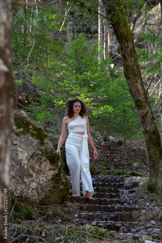 Portrait of a young man as he descends from a mountain stone staircase. The barefooted brunette girl with wavy brown hair wears a white playsuit with top and pants. Concept of communion with nature.