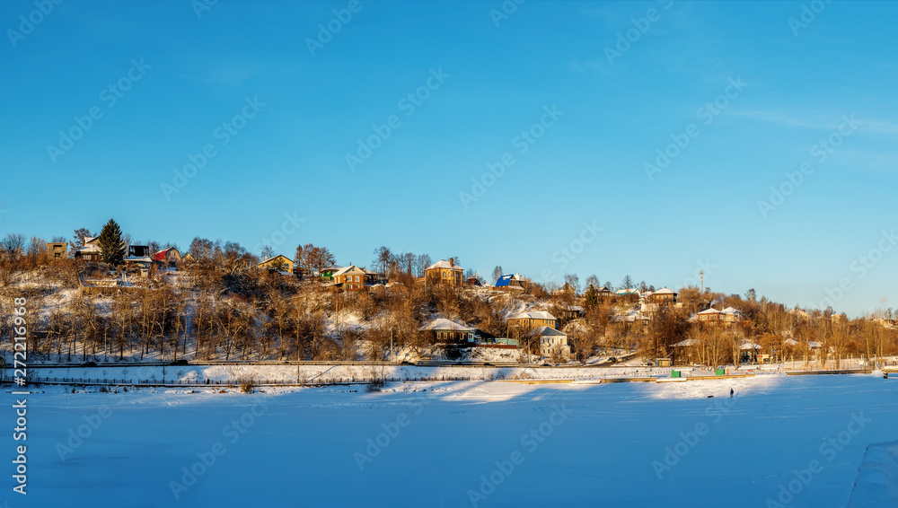 Before us is a panorama of the snow-covered surface of a frozen pond on the outskirts of the city of Perm. Behind the pond on the hill are low houses. Sunny winter's day.