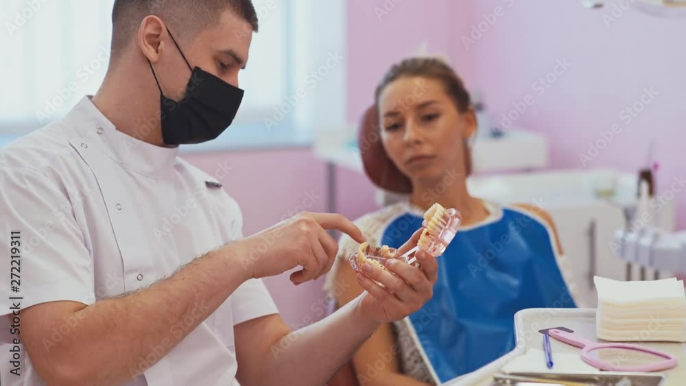 Dental care concept. Dentist showing plastic model of teeth to his female patient. Consultation at dental clinic Dental care concept. Dentist showing plastic model of teeth to his female patient. Consultation at dental clinic