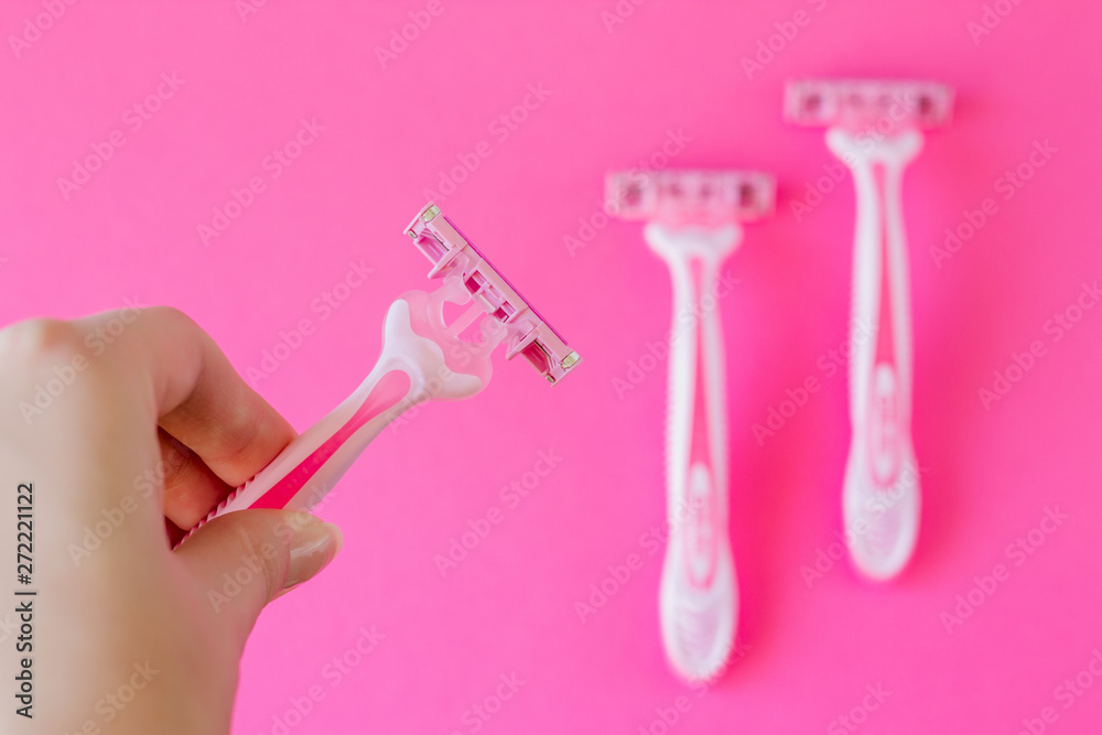 Pink razor in a female hand on a pink minimalistic background. Razor for personal hygiene for hair removal Pink razor in a female hand on a pink minimalistic background. Razor for personal hygiene for hair removal