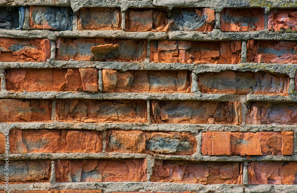 Cracked vintage orange bricks in the wall with cement masonry close-up