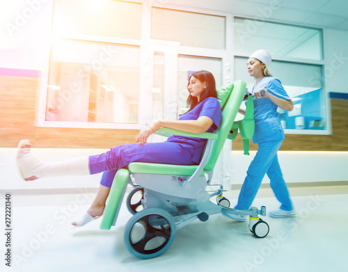 Nurse moves mobile medical chair with patient at hospital. Medical equipment.