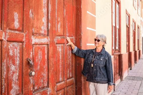 People touching one closed red and old door. Rustic wooden windows and dors from spanish tradition. One caucasian senior woman enjoying the trip