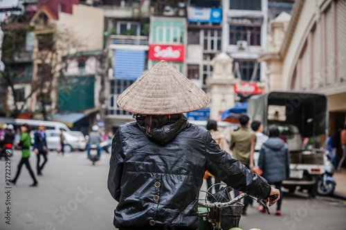 Woman walking with bicycle in Hanoi, Vietnam wearing traditional conical hat